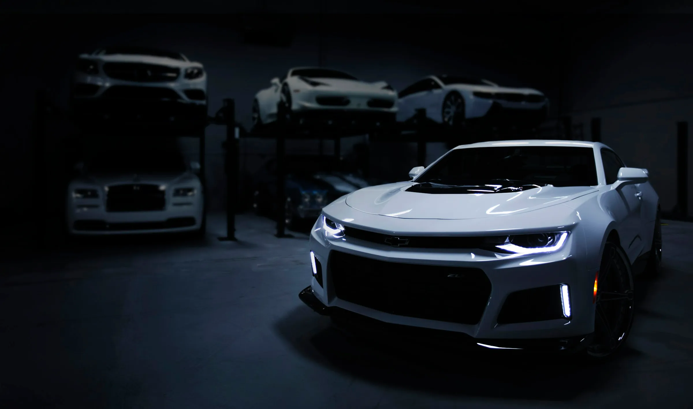 A silver Camaro parked in a dark detailing workshop under low directional light